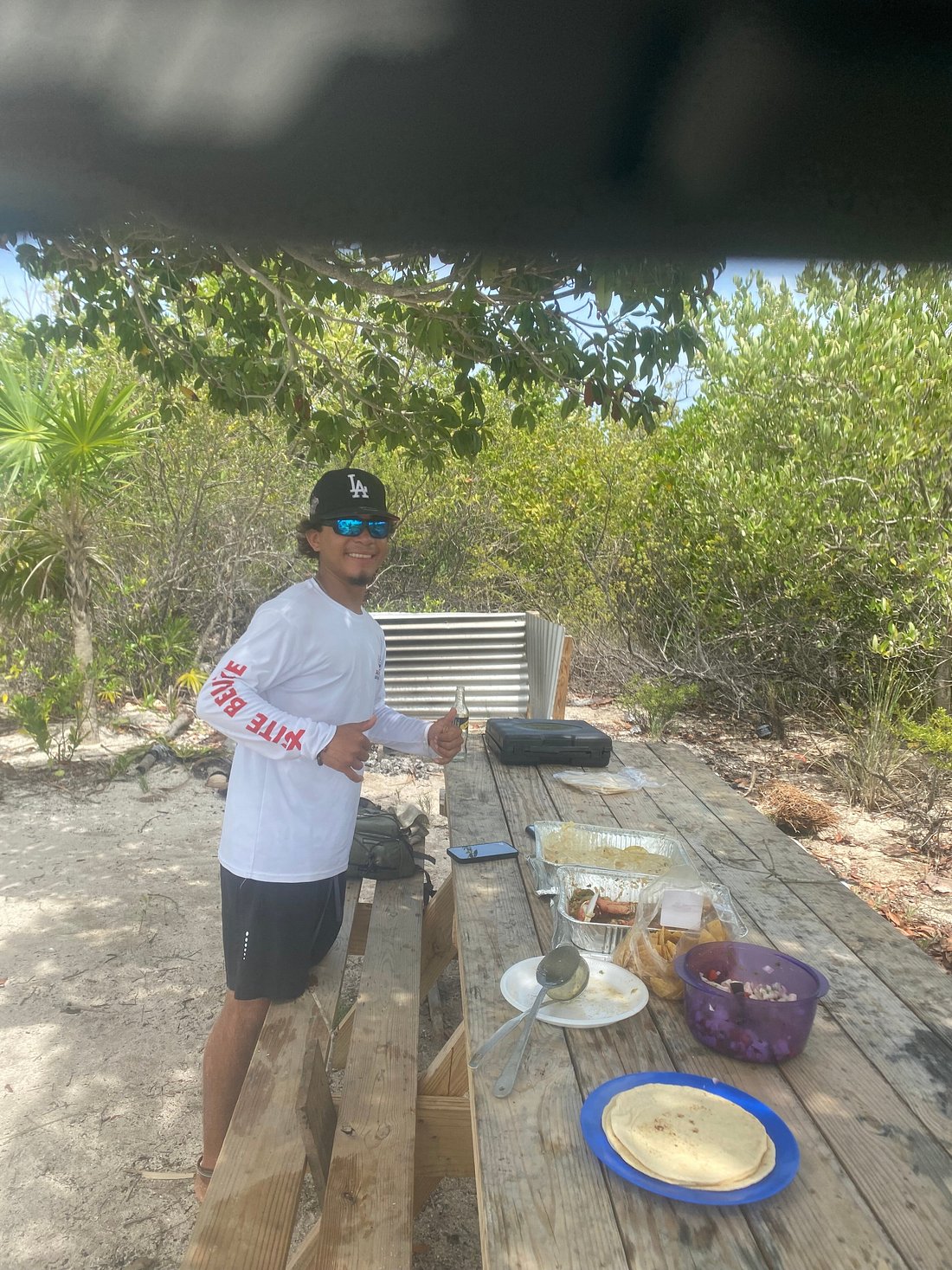 Local guide preparing a beach BBQ lunch at a shaded picnic table
