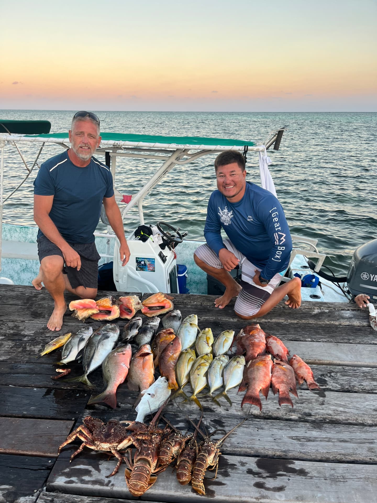 Captain and guest on the dock at sunset with a full haul of snapper, conch and spiny lobster