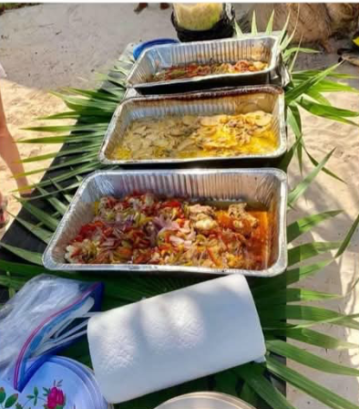 Trays of fresh ceviche, grilled fish and sides laid out on palm leaves for a beach lunch